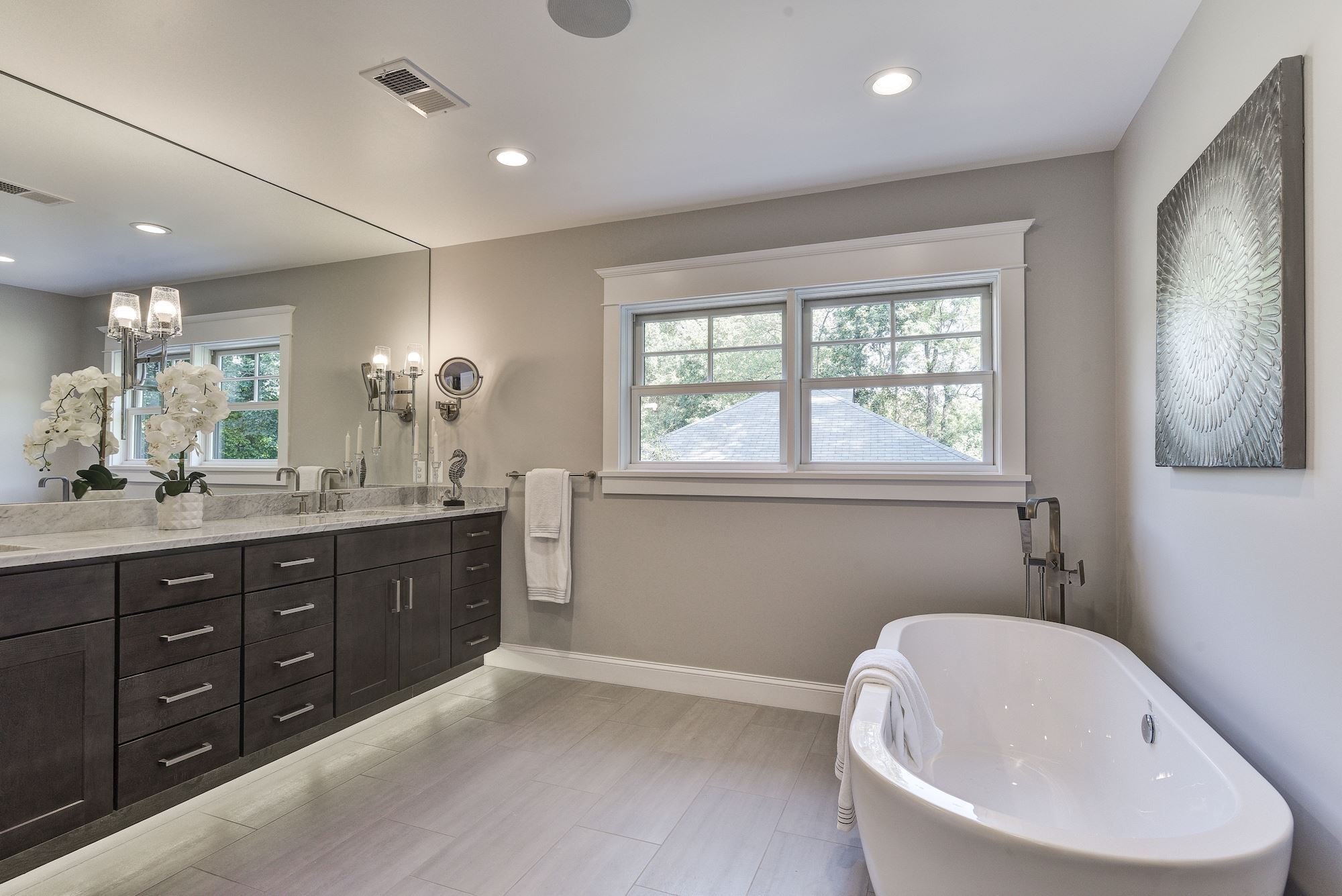 <img alt="Bright modern bathroom in Bethesda with a large mirror, award-winning dark wood double-sink vanity, a slipper tub, and windows letting in natural light." 