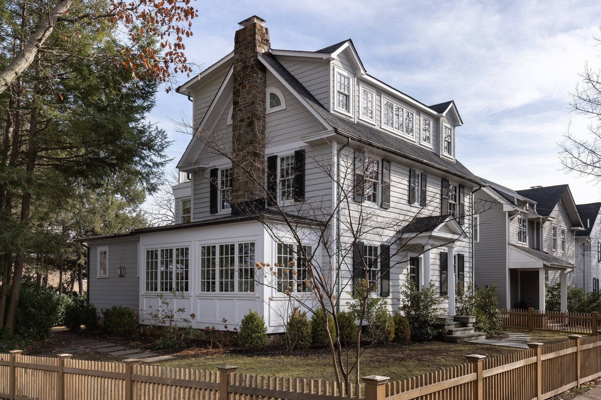 <img alt="A large, three-story white house with black shutters and a gray roof—expertly updated by Smiley Renovations—sits behind a wooden picket fence and bare trees on a quiet Northwest DC suburban street." src="#" />