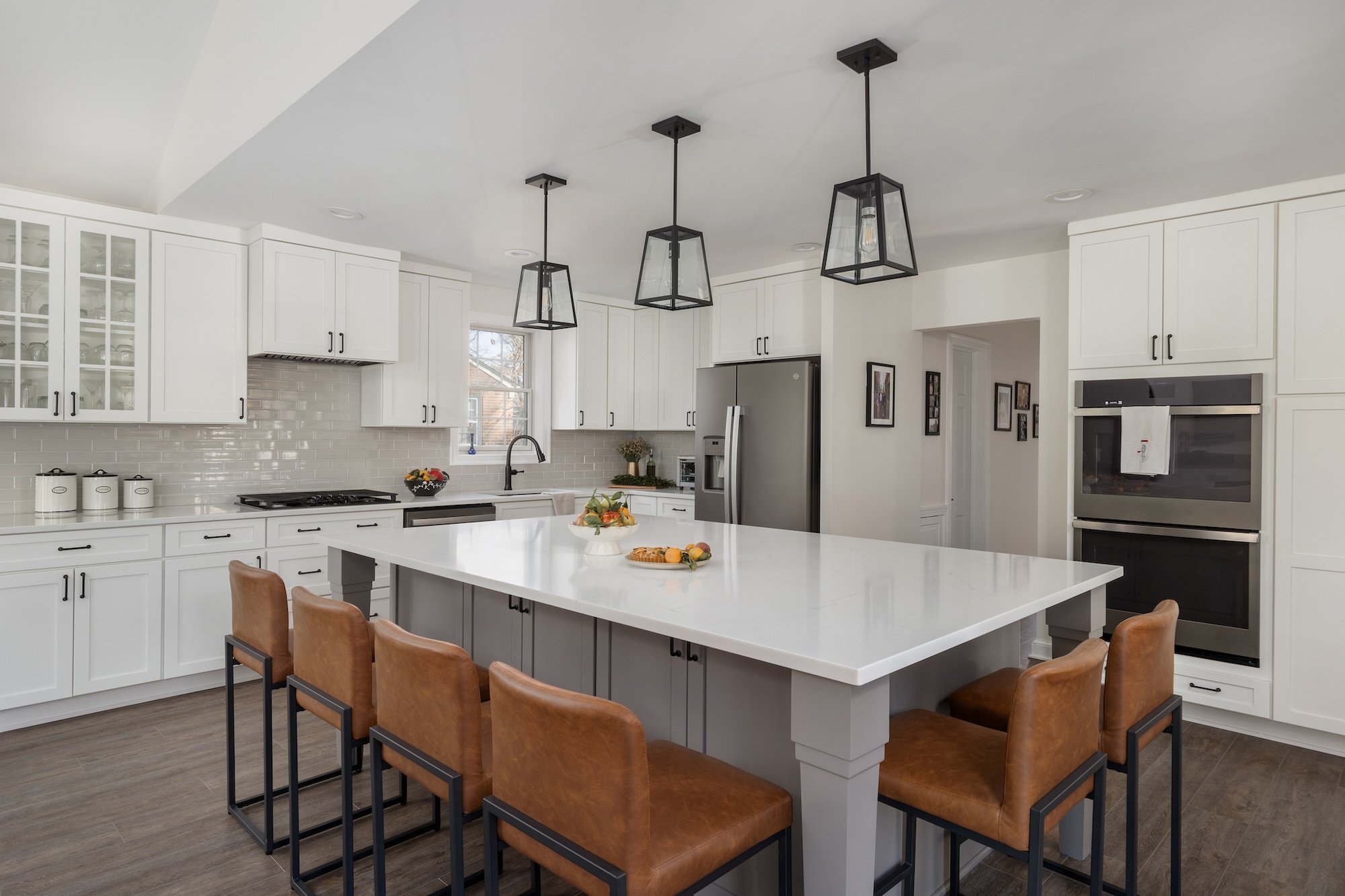 <img alt="Award-winning modern kitchen in Bethesda featuring white cabinets, stainless steel appliances, a large island with white countertop, brown leather barstools, pendant lighting, and dark wood flooring. Cozy seating area visible on the left." src="#" />