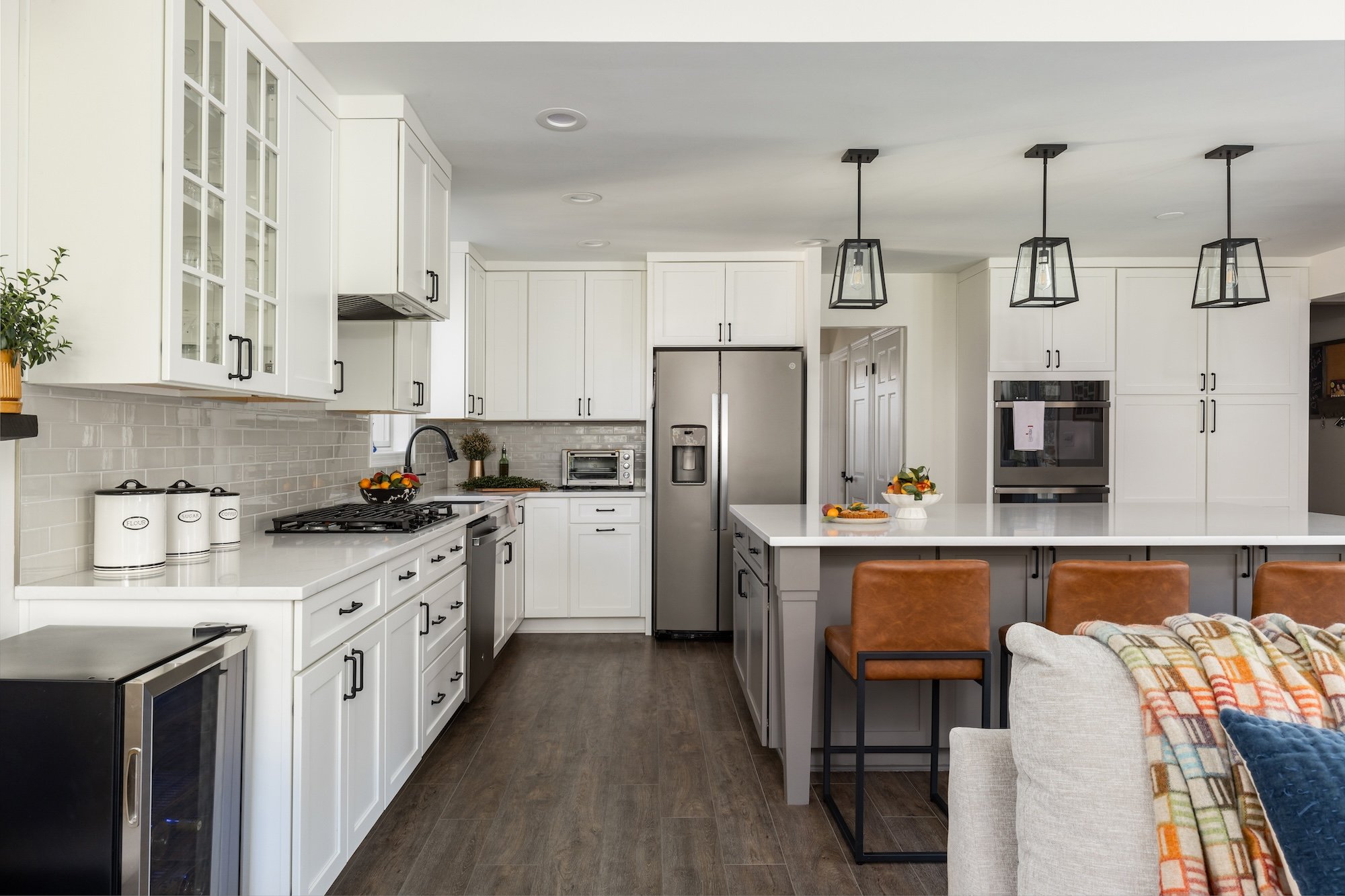 <img alt="Award-winning modern kitchen in Bethesda featuring white cabinets, stainless steel appliances, a large island with white countertop, brown leather barstools, pendant lighting, and dark wood flooring. Cozy seating area visible on the left." src="#" />