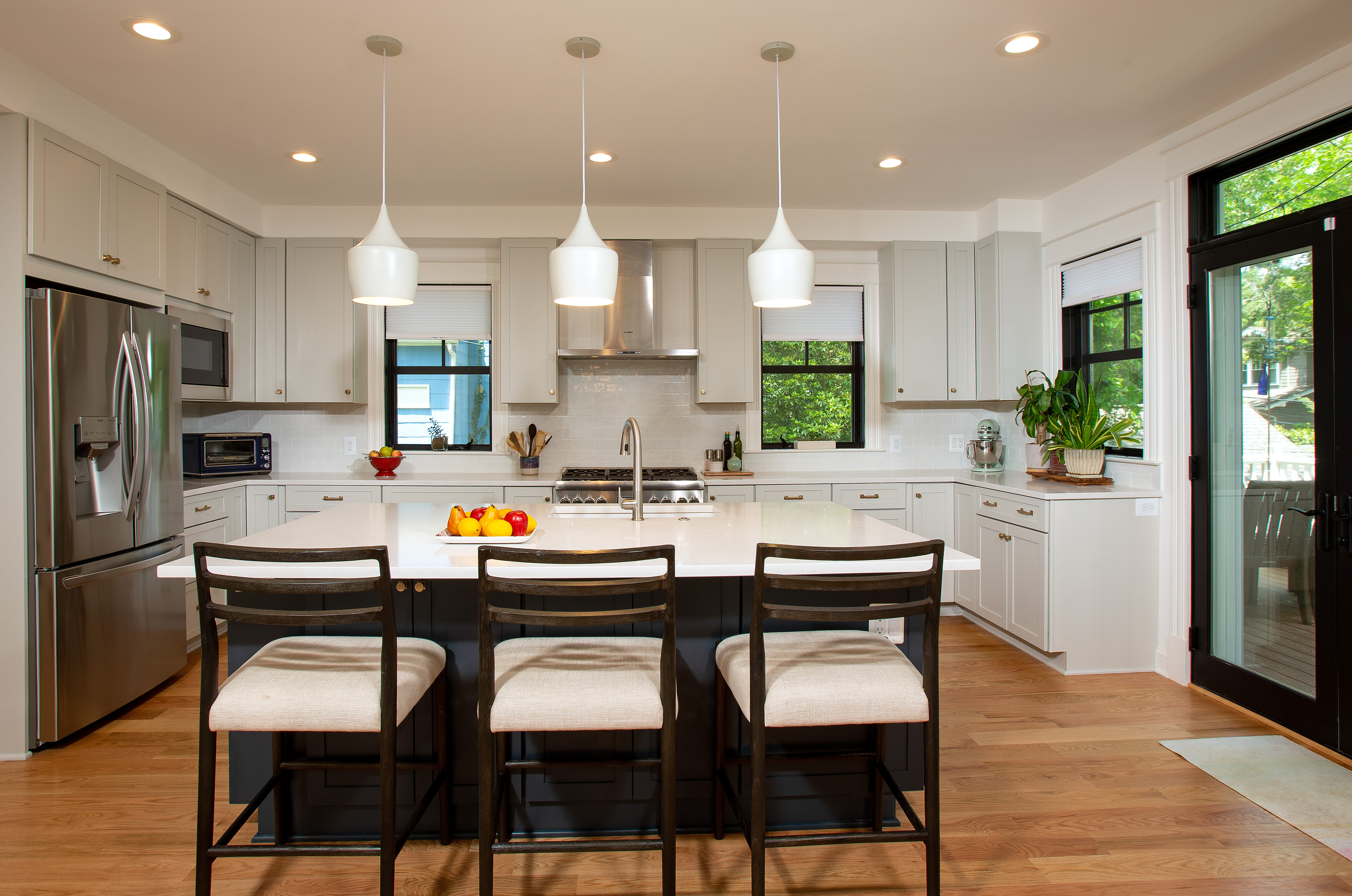 A bright kitchen featuring white cabinets, a spacious countertop, and a dining room table with chairs. The room includes large windows allowing natural light in, creating a warm and inviting atmosphere.