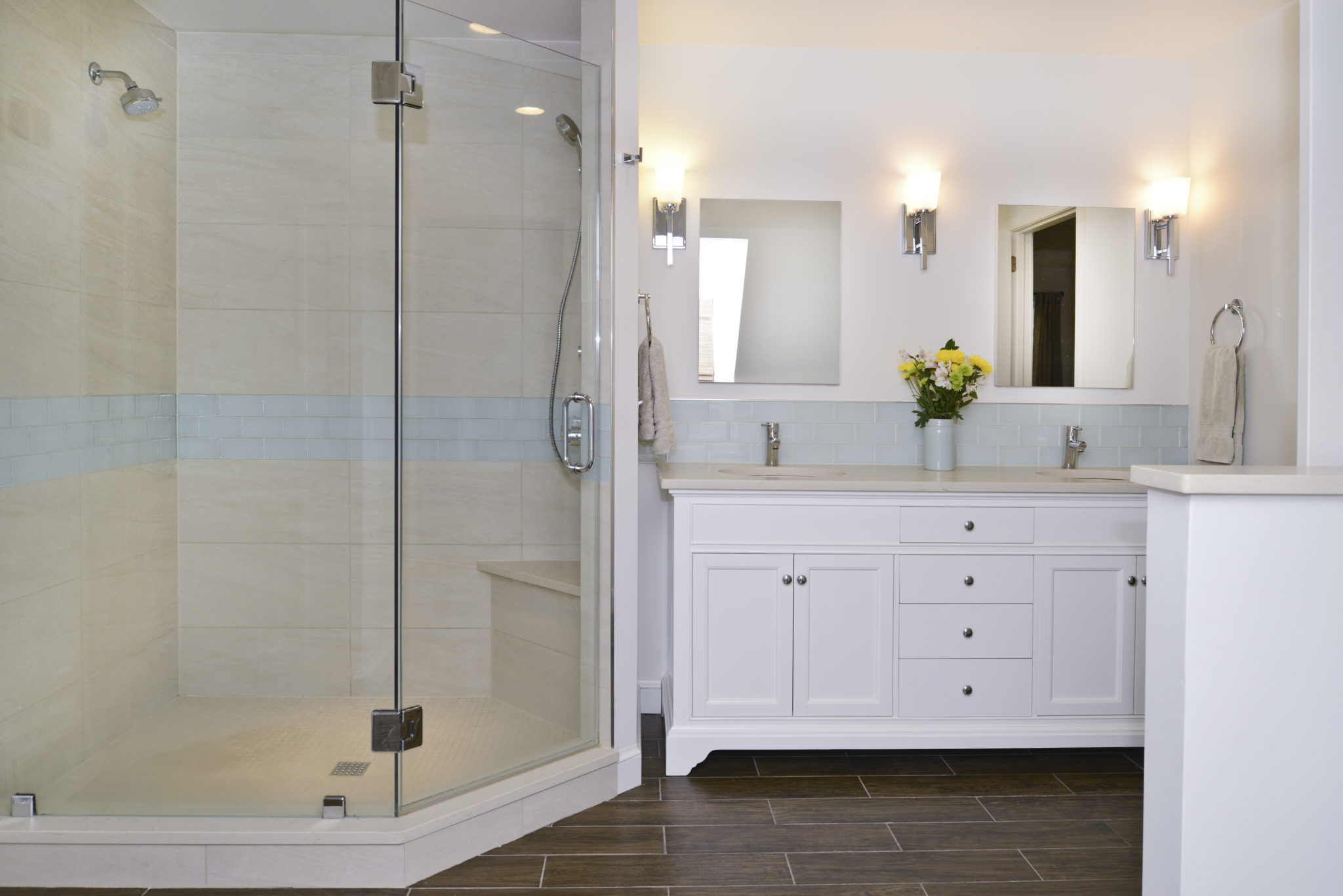 A modern bathroom featuring a glass shower, a bathtub, sink, mirror, and stylish cabinetry. The walls are tiled and the room is well-lit, showcasing a clean and contemporary design.