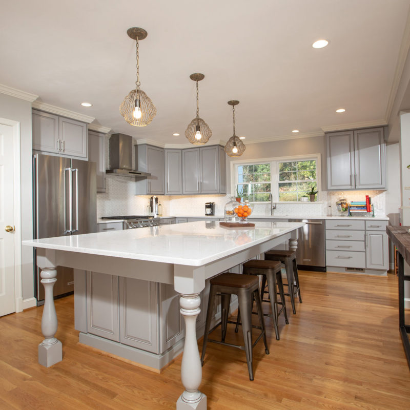 A contemporary kitchen featuring a white island in the center, surrounded by grey cabinetry and countertops. The setup includes a sink and various kitchen appliances, complemented by stylish furnishings and an inviting interior design.