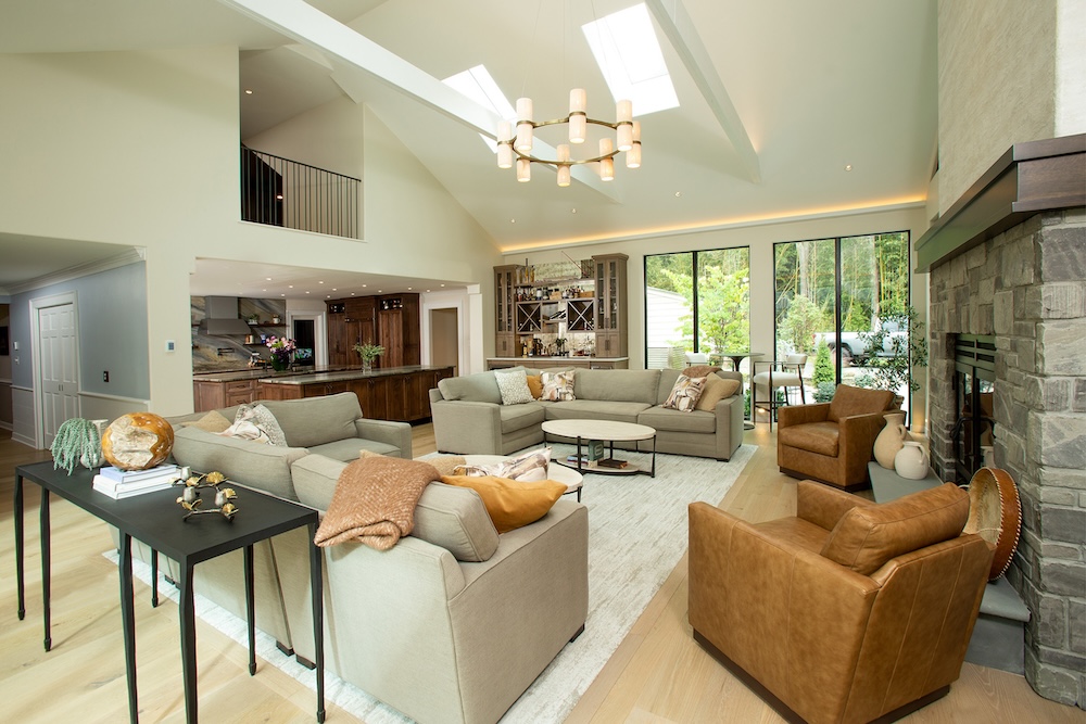 A spacious, modern living room in a Montgomery County home features large windows, skylights, two beige sofas, a central fireplace, and views of a lush garden. Natural light fills this award-winning remodeler’s bright and airy space.
