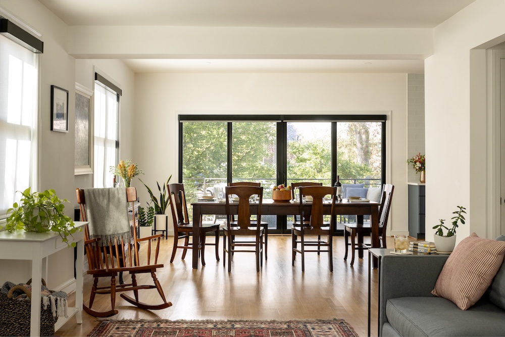 A modern dining area with wooden floors, a large dining table for six, and big windows. This Northwest DC remodeling project features sliding glass doors opening to a patio with outdoor seating.